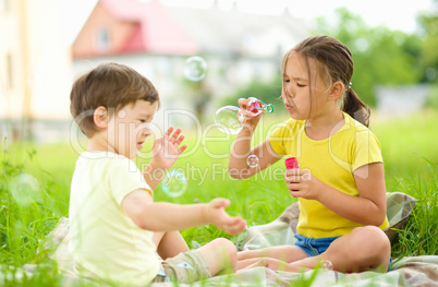 Little girl and boy are blowing soap bubbles