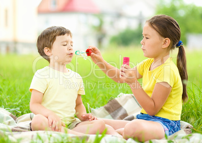 Little girl and boy are blowing soap bubbles