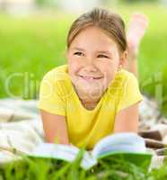 Little girl is reading a book outdoors