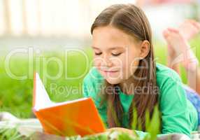 Little girl is reading a book outdoors