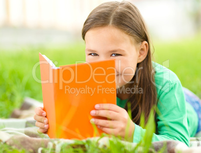 Little girl is reading a book outdoors