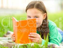 Little girl is reading a book outdoors