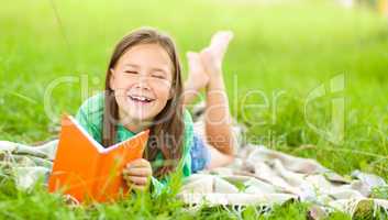 Little girl is reading a book outdoors