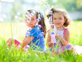 Two little girls are blowing soap bubbles