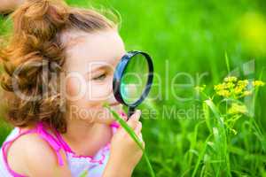 Young girl is looking at flower through magnifier