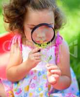 Young girl is looking at flower through magnifier