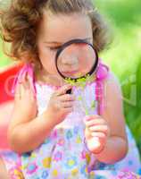 Young girl is looking at flower through magnifier