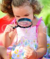 Young girl is looking at flower through magnifier