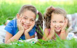 Two little girls are laying on green grass