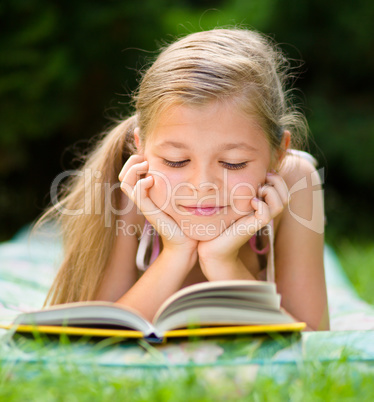 Little girl is reading a book outdoors