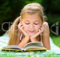 Little girl is reading a book outdoors