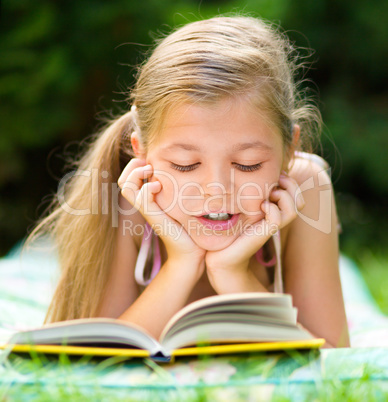 Little girl is reading a book outdoors