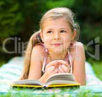 Little girl is reading a book outdoors