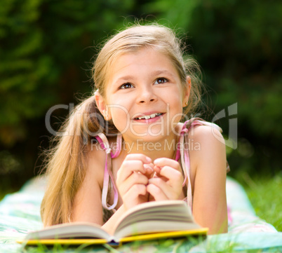 Little girl is reading a book outdoors