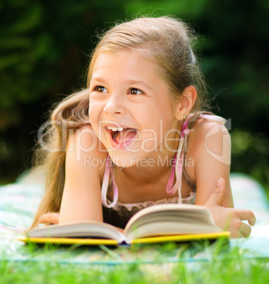 Little girl is reading a book outdoors