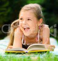 Little girl is reading a book outdoors