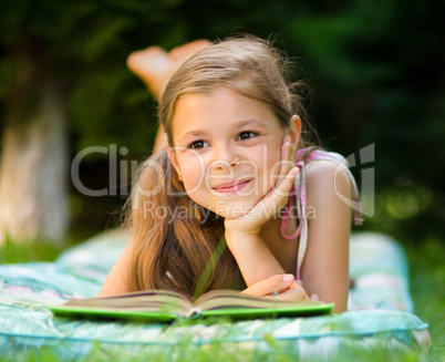 Little girl is reading a book outdoors