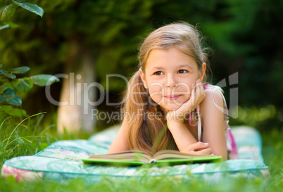 Little girl is reading a book outdoors