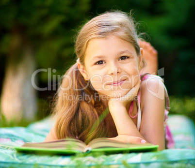 Little girl is reading a book outdoors