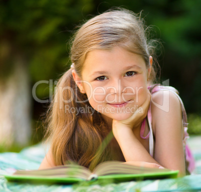 Little girl is reading a book outdoors