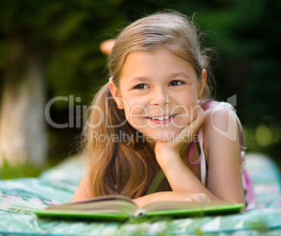 Little girl is reading a book outdoors