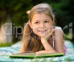 Little girl is reading a book outdoors