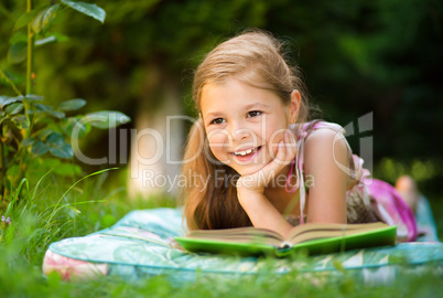 Little girl is reading a book outdoors