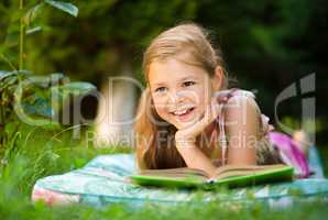 Little girl is reading a book outdoors