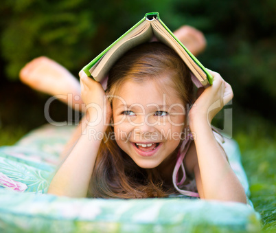 Little girl is hiding under book outdoors