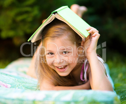 Little girl is hiding under book outdoors