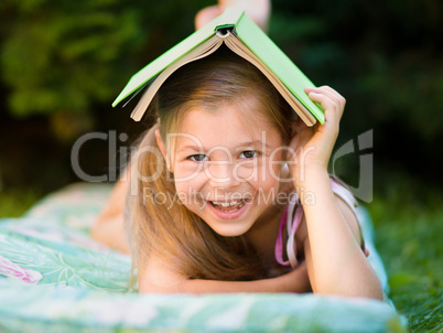 Little girl is hiding under book outdoors