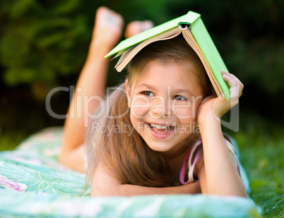 Little girl is hiding under book outdoors