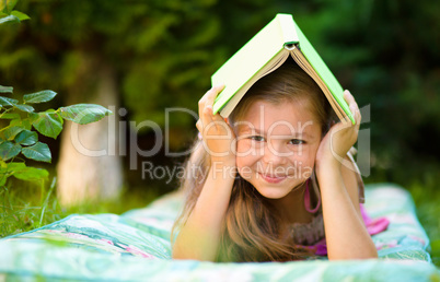 Little girl is hiding under book outdoors