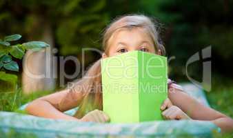 Little girl is hiding behind book outdoors
