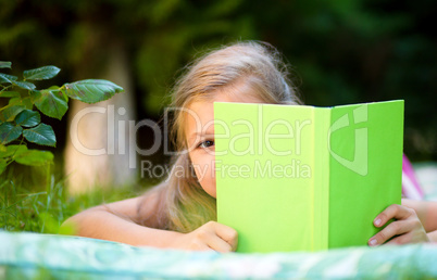 Little girl is hiding behind book outdoors