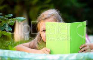 Little girl is hiding behind book outdoors