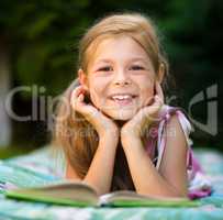 Little girl is reading a book outdoors