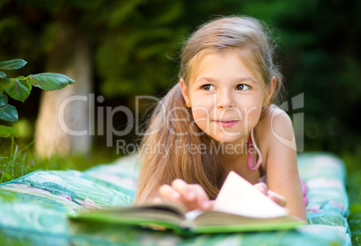 Little girl is reading a book outdoors