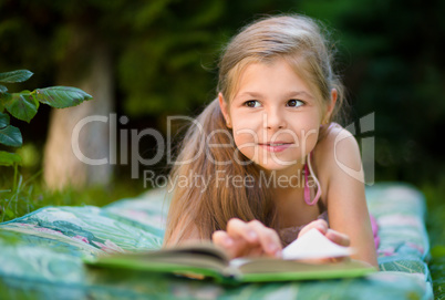 Little girl is reading a book outdoors