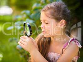 Young girl is looking at flower through magnifier