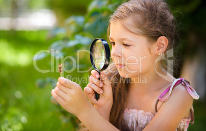 Young girl is looking at flower through magnifier