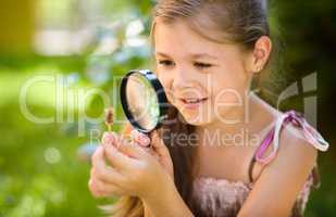 Young girl is looking at flower through magnifier