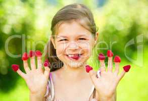 Young girl is holding raspberries on her fingers