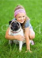 Little girl and her pug dog on green grass