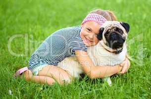 Little girl and her pug dog on green grass