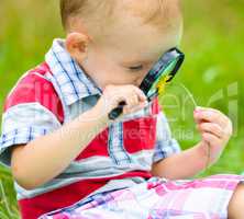 Young boy is looking at flower through magnifier