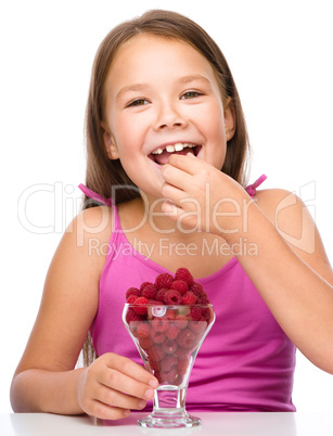 Happy little girl is eating raspberries