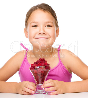 Happy little girl is eating raspberries