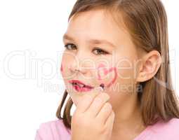 Little girl is applying lipstick on her cheek