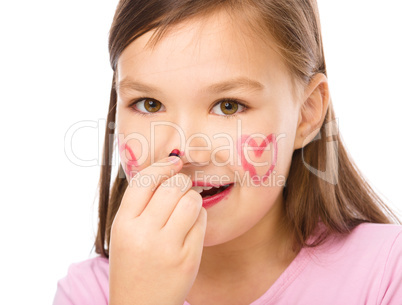 Little girl is applying lipstick on her nose